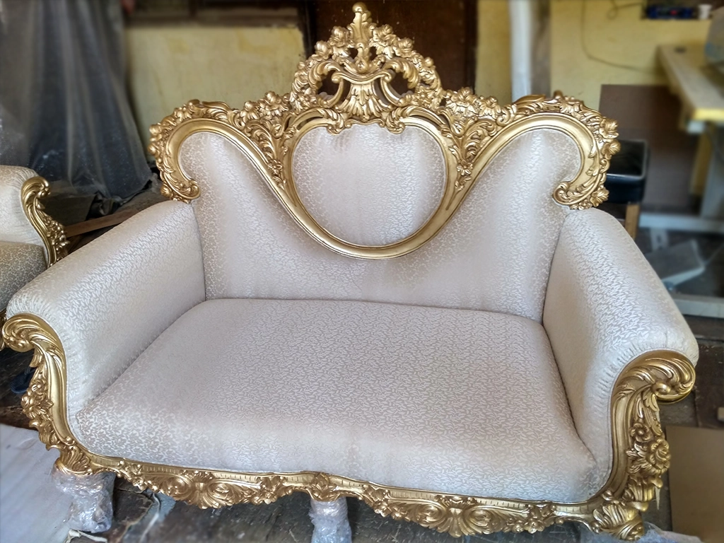 A maharaja style white color leatherette and gold color carving finish sofa for living area.