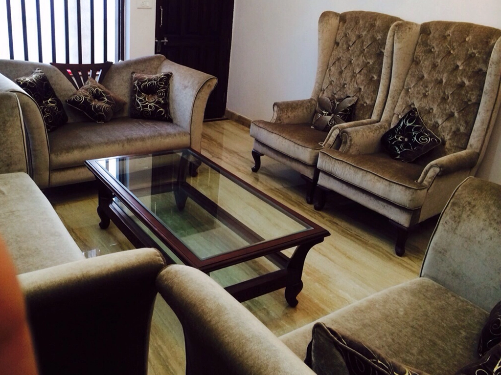 A brown color velvet sofa with two high back chair with one glass top center table for living hall area.