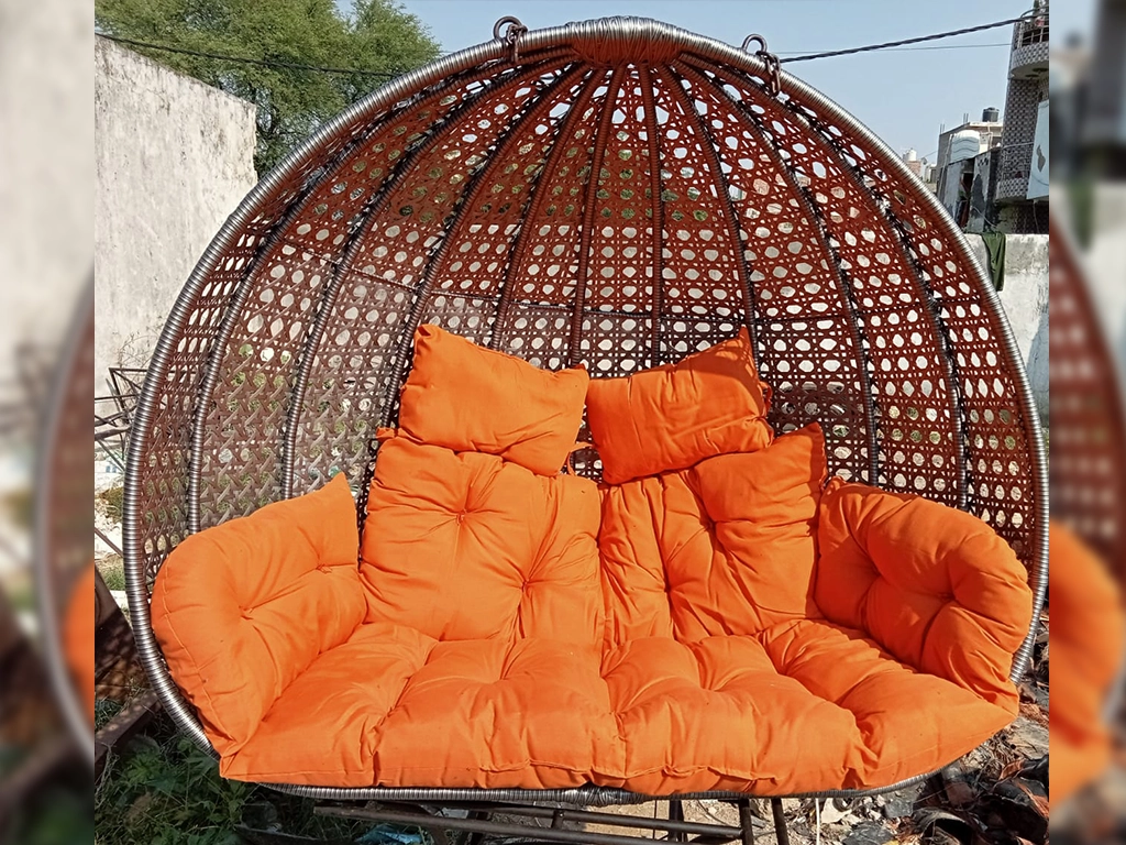 grey color two seater swing chair with orange color cushion for balcony area.