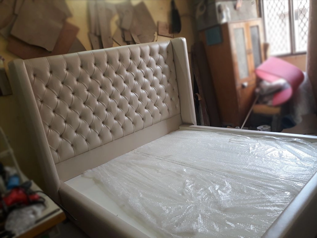 a diamond design quilted work on head side of double bed in white color for bedroom.