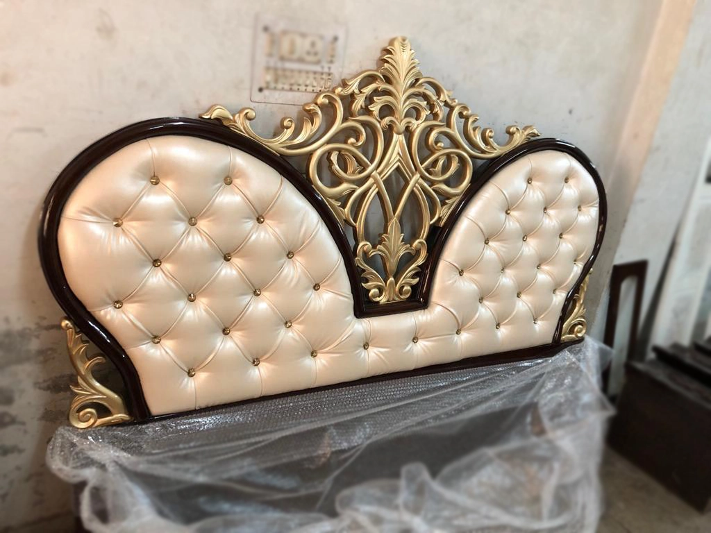 A heart shape beige color leatherette cushioned bed side with gold carving work .