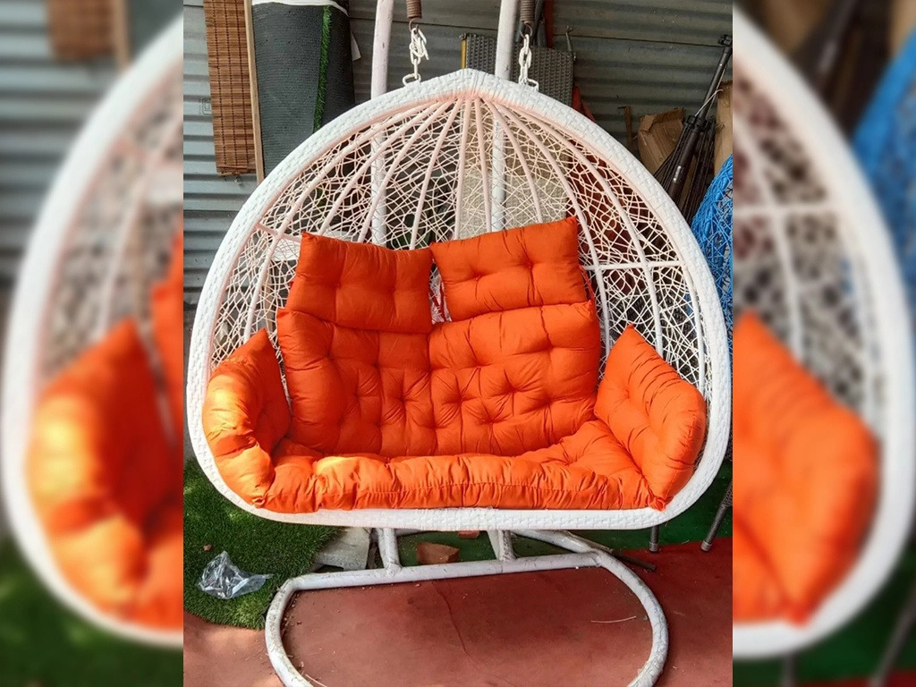 White color two seater swing chair with orange color cushion for balcony area.