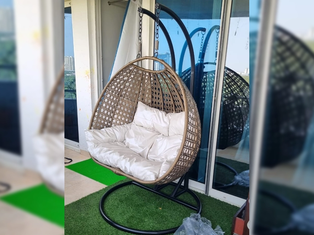 Beige color two seater swing chair with white color cushion for balcony area.